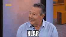 a man in a blue shirt is smiling with the word klar written on his face .