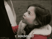 a little girl in a red jacket is holding a piece of paper in her hand and says hmmkay .