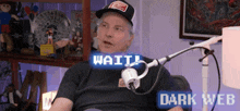 a man wearing a hat is sitting in front of a microphone with the words wait dark web above him