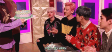 a group of young men are sitting around a cake and one of them says it 's okay ..
