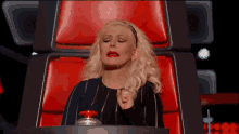 a woman is sitting in a red chair with her eyes closed and a red button in her hand .