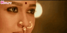 a close up of a woman 's face with a nose ring and a red dot on her forehead .