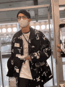 a man wearing a mask and glasses is standing in front of a door with the name kiokio on it