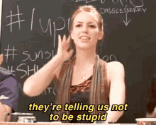 a woman says they 're telling us not to be stupid in front of a chalkboard