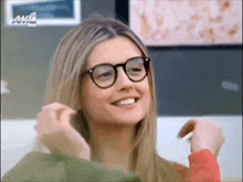 a woman wearing glasses and a red shirt is smiling and adjusting her hair .