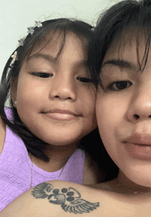 a woman and a little girl are posing for a picture and the little girl has a tattoo of a paw print on her shoulder