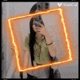 a woman is taking a selfie in front of a mirror with an orange frame around her .