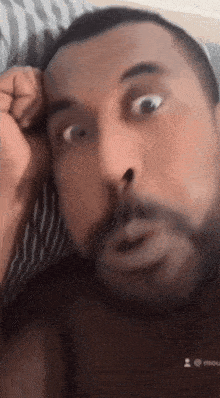 a man with a beard is laying on a bed and making a funny face