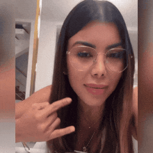 a woman wearing glasses and a necklace is pointing at her finger