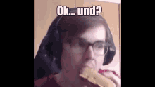 a man wearing headphones and glasses is eating a sandwich .