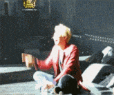 a man in a red jacket is sitting on a stage with his legs crossed