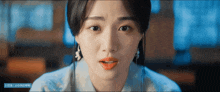 a close up of a woman 's face with a blue banner behind her that says ' a ' on it