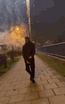 a man is standing on a sidewalk in front of a firework display