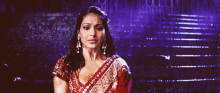 a woman in a red and gold saree is standing in front of a set of stairs .
