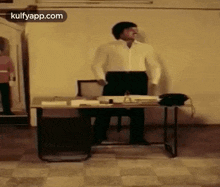 a man in a white shirt is standing in front of a desk with a phone on it .