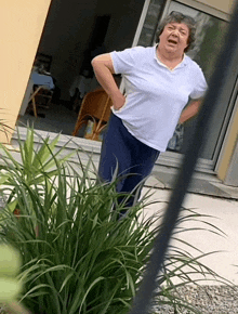 a woman in a white shirt and blue pants stands in front of a window