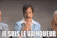 a man with a mustache is sitting in front of a group of people and says `` je suis le vainqueur ''