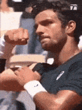 a man in a blue shirt is flexing his muscles while wearing a white wristband .