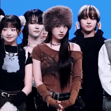 a group of young women are standing next to each other on a blue background . one of the girls is wearing a fur hat .