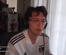 a young man wearing glasses and headphones is sitting in front of a computer screen .
