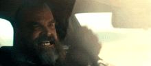 a man with a beard is driving a car and making a face
