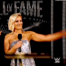 a woman in a silver dress is holding a microphone in front of a sign that says fame .
