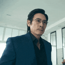 a man wearing glasses and a blue suit is looking at the camera