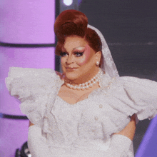 a drag queen wearing a white dress and pearls is smiling