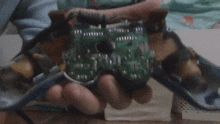 a person is holding a broken video game controller with a green board