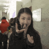 a woman wearing a black jacket and black gloves is making a heart shape with her hands