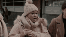 a woman wearing a knitted hat and scarf is standing in front of a building