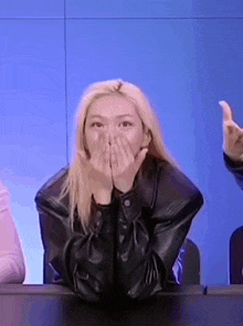 a woman in a leather jacket is covering her mouth with her hands .