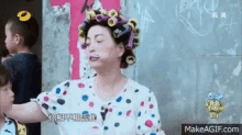 a woman with curlers on her head is standing in front of a wall .