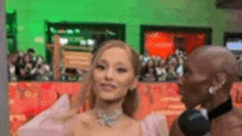 a woman in a pink dress is talking to a man in a suit in front of a microphone .
