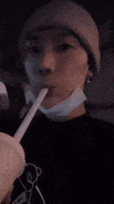 a man wearing a beanie is drinking from a cup with a straw .
