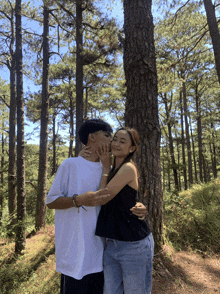 a man kisses a woman on the cheek in front of a pine tree