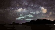 a night sky filled with lots of stars and clouds over a body of water