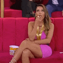 a woman is sitting on a couch eating popcorn .