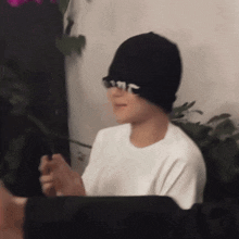 a person wearing a white shirt and a black beanie with a white letter t on it