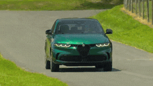 a green alfa romeo is driving down a country road