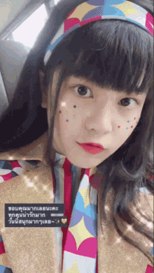 a girl wearing a colorful headband and tie looks at the camera with a heart in the lower right corner