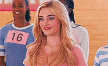 a group of girls are standing next to each other in a gym . one of the girls is wearing a number 16 shirt .