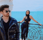 a man wearing sunglasses stands next to a woman wearing a scarf