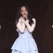 a woman in a blue dress is singing into a microphone while standing on a stage .