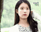 a woman holds her hand to her ear in front of a sign that says ' 아이유 ' on it