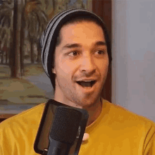 a man wearing a beanie and a yellow shirt is speaking into a microphone