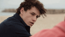 a young man with curly hair is sitting on a beach with the words jayanedna below him