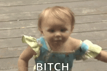 a baby in a blue dress is walking on a wooden deck and says bitch .