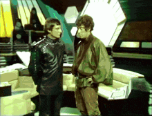 two men are standing next to each other in a room and one of them has a green jacket