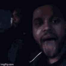 a man sticking his tongue out while another man looks on ..